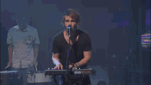 a man singing into a microphone while playing an aka moniak keyboard