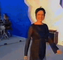 a woman in a black dress stands in front of a blue wall