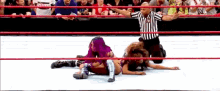 two women are wrestling in a ring while a referee looks on
