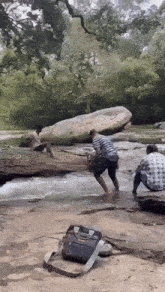 a man is jumping into a river while another man sits on a rock in the background .