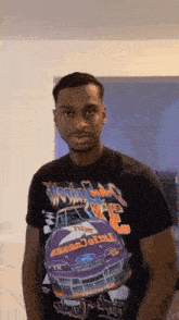 a young man wearing a black t-shirt with a purple race car on it is standing in a room .