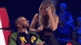 a woman is touching a man 's hair while wearing a jacket with kp on it