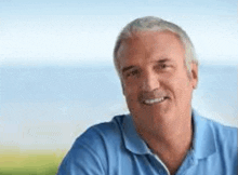 a man in a blue shirt is smiling for the camera while sitting outside .