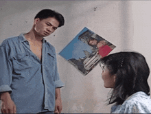 a man in a blue shirt is standing next to a woman with a picture on the wall behind them