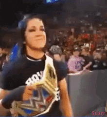 a woman wearing a black shirt with the word row on it is holding a wrestling championship belt