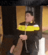 a man in a yellow and black jacket is standing in front of a wall with nyrhythm.com written above him