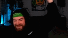 a man with a beard wearing headphones and a green headband is dancing in a dark room .