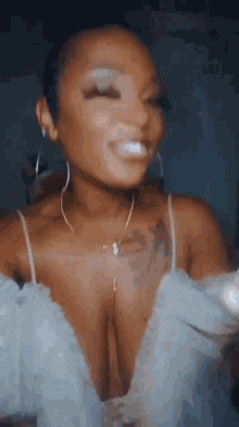 a woman with a tattoo on her chest is wearing a white dress and earrings and smiling .