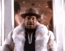 a man wearing a fur coat and a hat stands in front of a window .