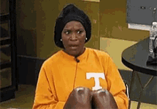a woman wearing a yellow shirt with the letter t on it is sitting at a table .