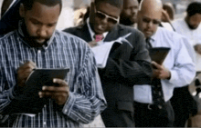a group of men are standing in a line looking at their phones