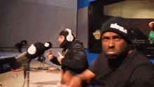 a man wearing headphones and a hat that says ' altitude ' on it stands in front of a microphone