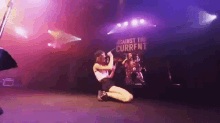 a woman is singing into a microphone on a stage with a sign that says against the current .