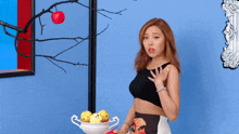 a woman in a black top stands in front of a bowl of fruit