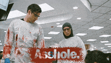 a man and a woman are standing next to each other with the word asshole written in red
