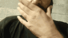 a man covering his mouth with his hand in a black shirt