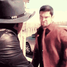 two men are standing next to each other and one is wearing a cowboy hat and a leather jacket .