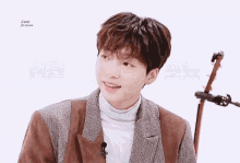 a young man wearing a brown jacket and a white turtleneck smiles for the camera