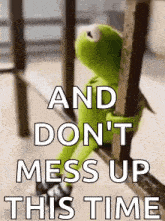 kermit the frog is sitting on a railing holding onto a railing .