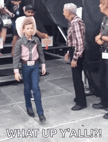 a young boy in a cowboy outfit is standing next to a man in a plaid shirt and the words what up y'all