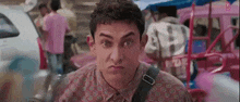 a man in a pink shirt is making a funny face while standing in front of a crowd of people .