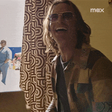 a man wearing sunglasses is laughing in front of a wall that says max on it