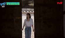 a woman in a white tank top and blue jeans is standing in front of a black wall .