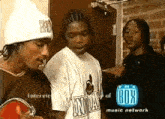 a group of young men are standing in front of a box music network advertisement