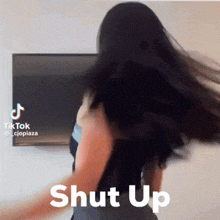a woman with long hair is dancing in front of a tv with the words shut up behind her