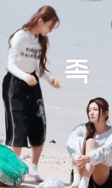 two girls are sitting on the beach and one of them is holding a yellow object .