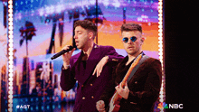 two men singing and playing a guitar on a stage with nbc written on the bottom