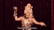 a woman in a costume is holding a light in her hand and says `` tranos is coming '' .