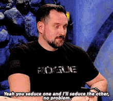 a man with a beard is wearing a black shirt that says yeah you seduce one and i 'll seduce the other