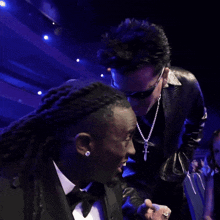 a man in a tuxedo stands next to another man with dreadlocks