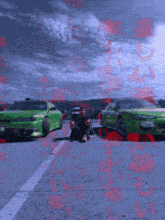 a man sits on the ground in front of two green cars one of which has a license plate that starts with the letter c
