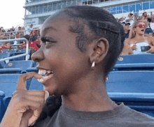 a woman is sitting in a stadium with a crowd behind her and smiling .
