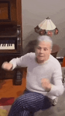 an elderly man is sitting on a couch with a lamp on his head and a piano in the background .