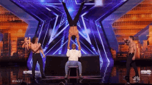a man is doing a handstand on a stool on a stage with a nbc logo in the background