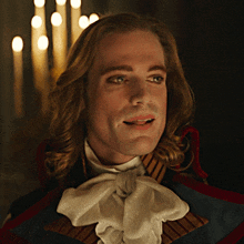 a man with long hair and a bow tie is smiling in front of candles