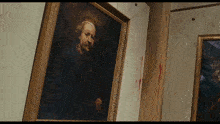 a painting of a man in a gold frame hangs on a wall with blood on it
