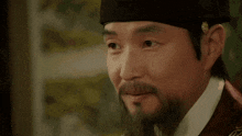 a man with a beard is wearing a hat and looking at something .
