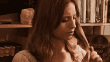 a woman is standing in front of a bookshelf holding her hair .
