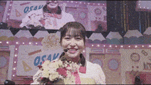 a woman is holding a bouquet of flowers and smiling in front of a screen that says osaka