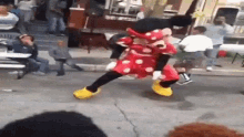 a mickey mouse mascot is dancing on the street in front of a crowd .