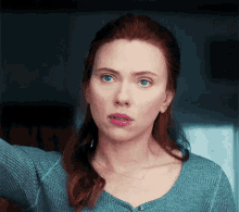 a close up of a woman 's face with red hair and blue eyes wearing a blue sweater .