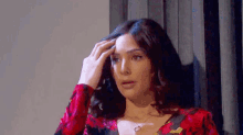a woman in a red floral dress is touching her hair and looking at the camera .