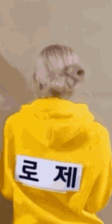 a woman wearing a yellow hoodie is standing in front of a wall and looking at the camera .