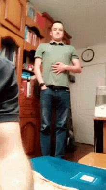 a man in a green shirt is standing in a living room with a clock on the wall