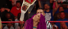 a woman with purple hair is holding a wrestling championship belt in a wrestling ring .