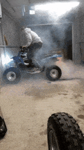 a man is riding a blue atv in a garage with smoke coming out of it